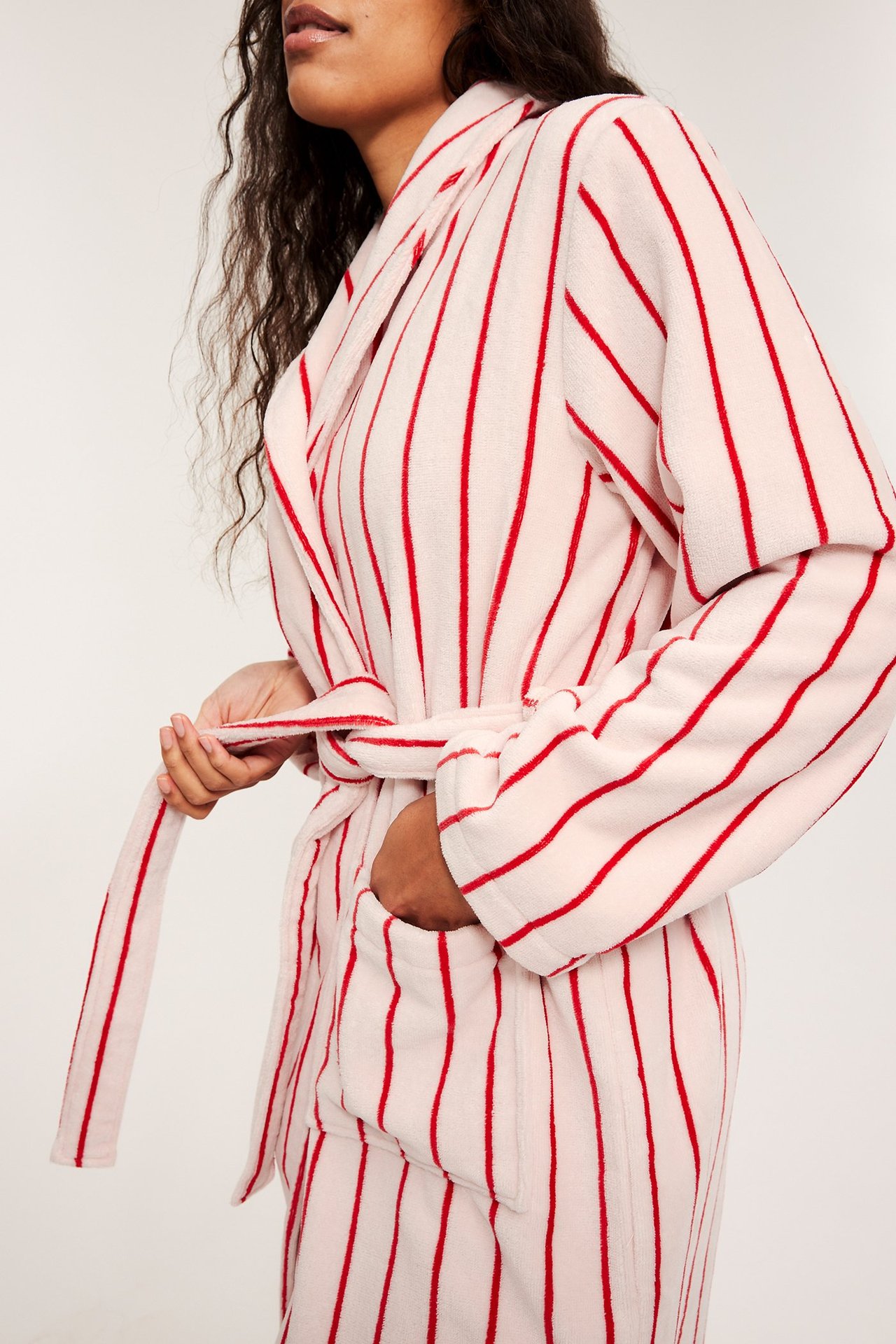 Nainen sitoo vaaleanpunaisen froteeaamutakin, jossa on punaisia raitoja, huivikaulus ja taskut, sivukuva.