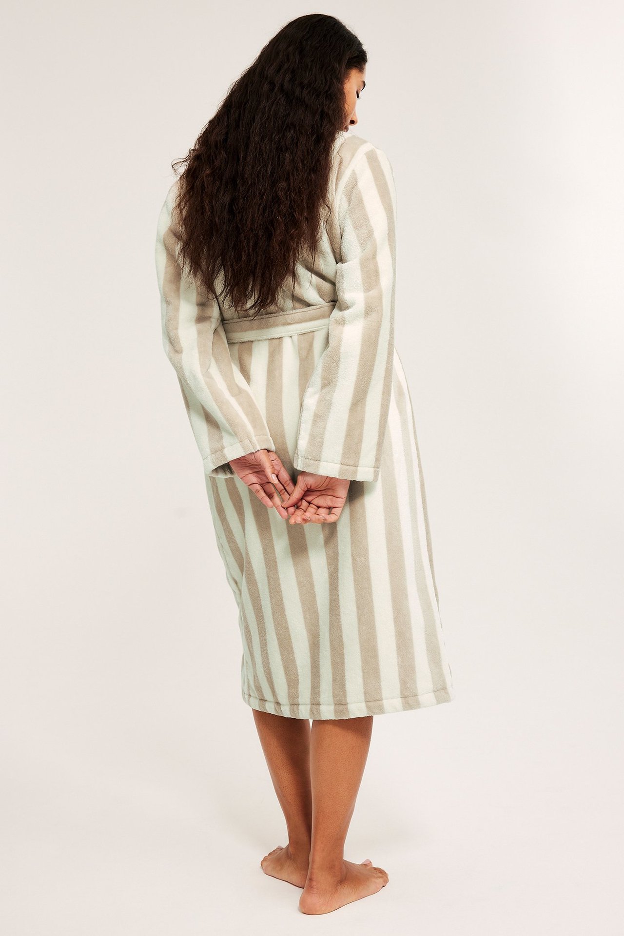 Kvinna sedd bakifrån i en ljusbeige och vitrandig morgonrock i bomullsfrotté med knytskärp.