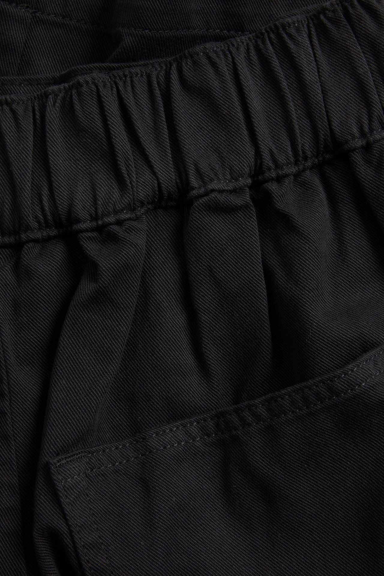 Lähikuva yksivärisistä mustista lyocell- ja puuvillabermuda-shortseista, joissa joustovyötärö ja taskuyksityiskohta.