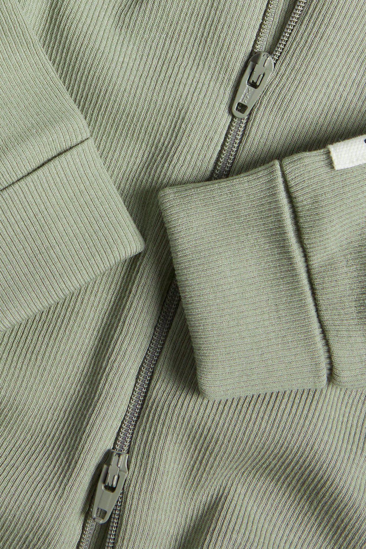 Zbliżenie ciemnozielonego, prążkowanego kombinezonu niemowlęcego z dwukierunkowym zamkiem i podwiniętymi mankietami.