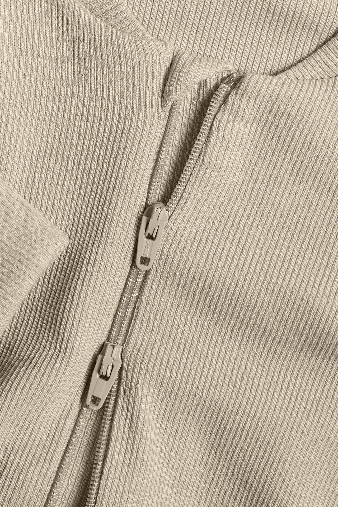 Närbild på en beige ribbad babyjumpsuit med tvåvägsdragkedja.