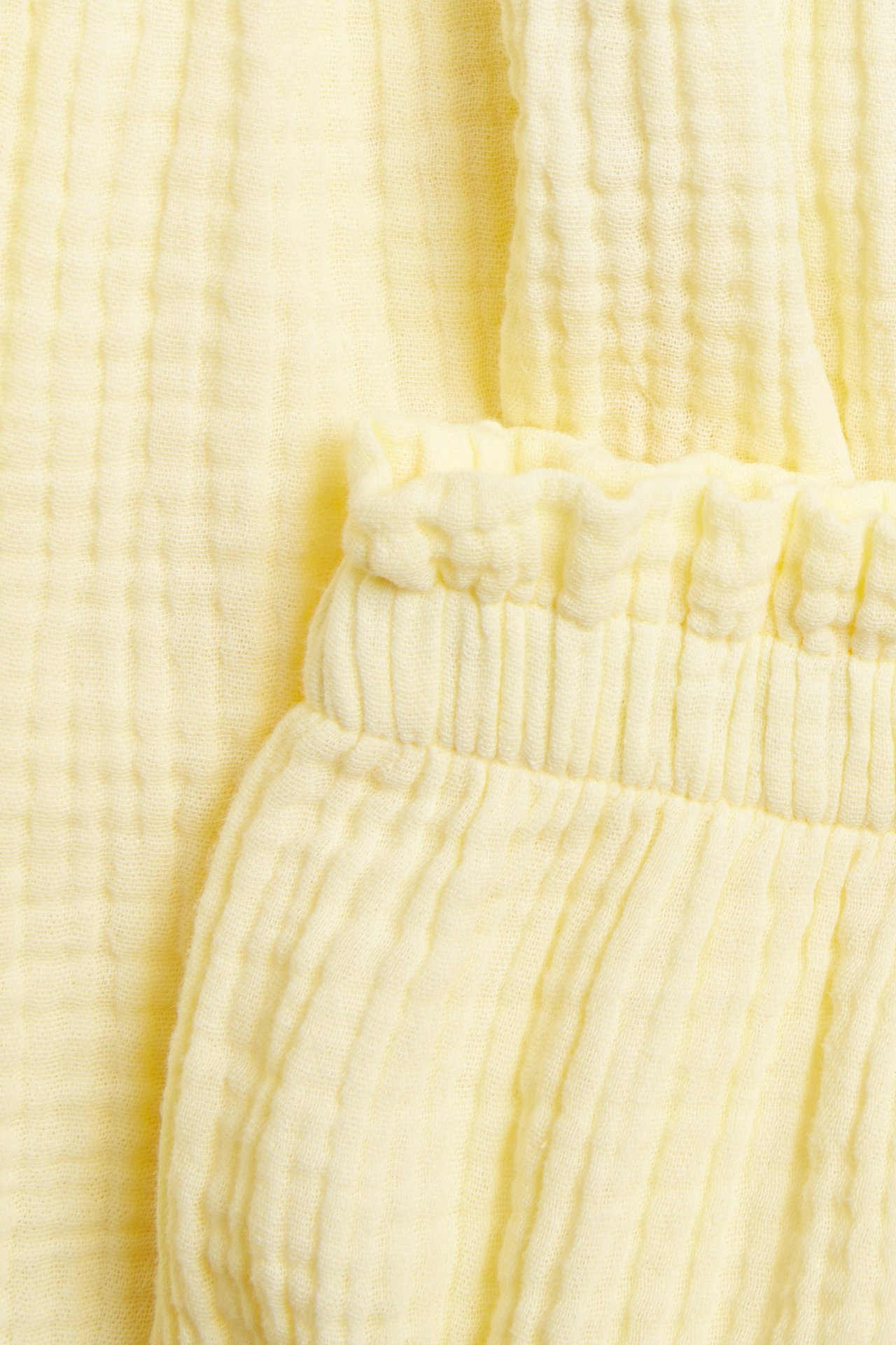 Zbliżenie jasnego żółtego zestawu muślinowego dla niemowląt, z marszczonym materiałem i elastyczną talią.