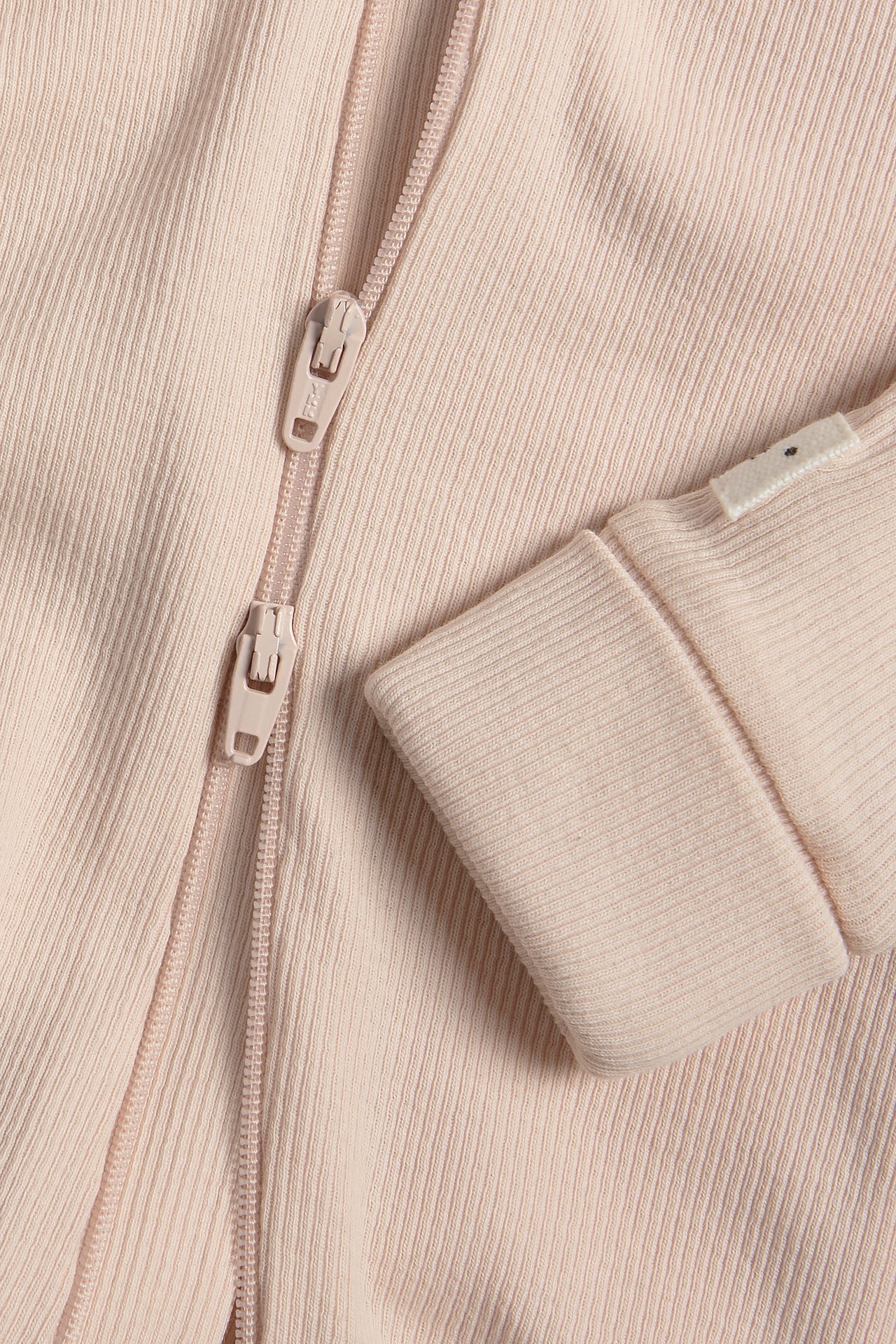 Närbild på en rosa ribbad babyjumpsuit med tvåvägsdragkedja och vikbara muddar.