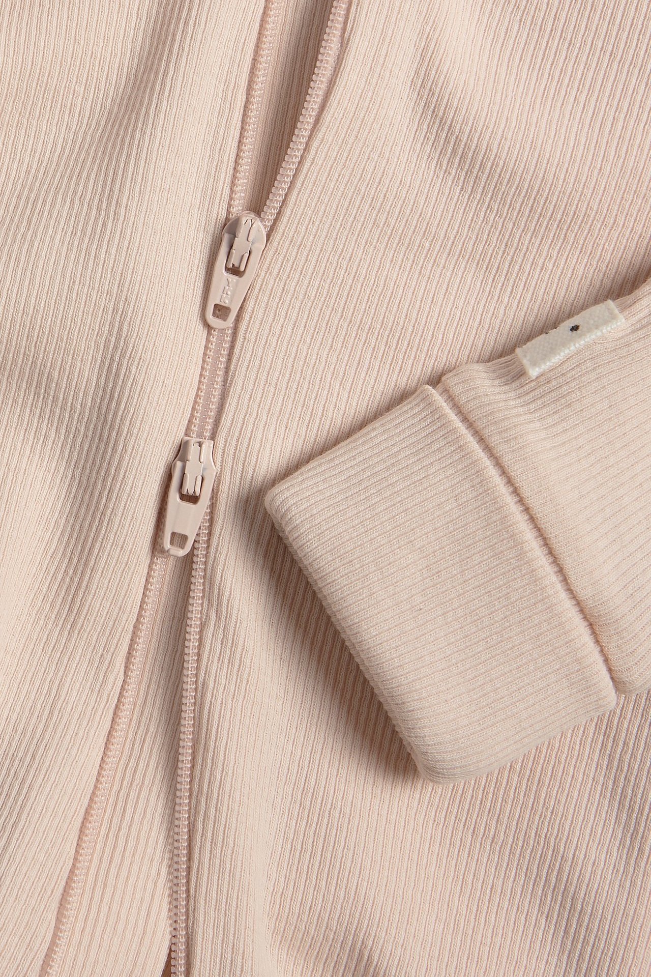 Lähikuva vaaleanpunaisesta ribbivauvanhaalarista, jossa kaksisuuntainen vetoketju ja taitettavat resorit.