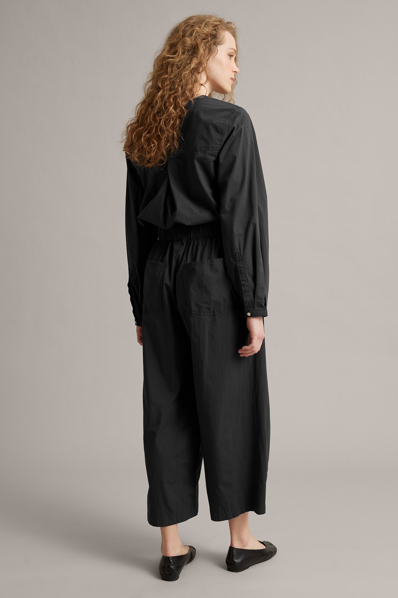 Naisen sivu/takakuva: mustat barrel-fit housut, joustovyötärö, musta paita, mustat ballerinas.