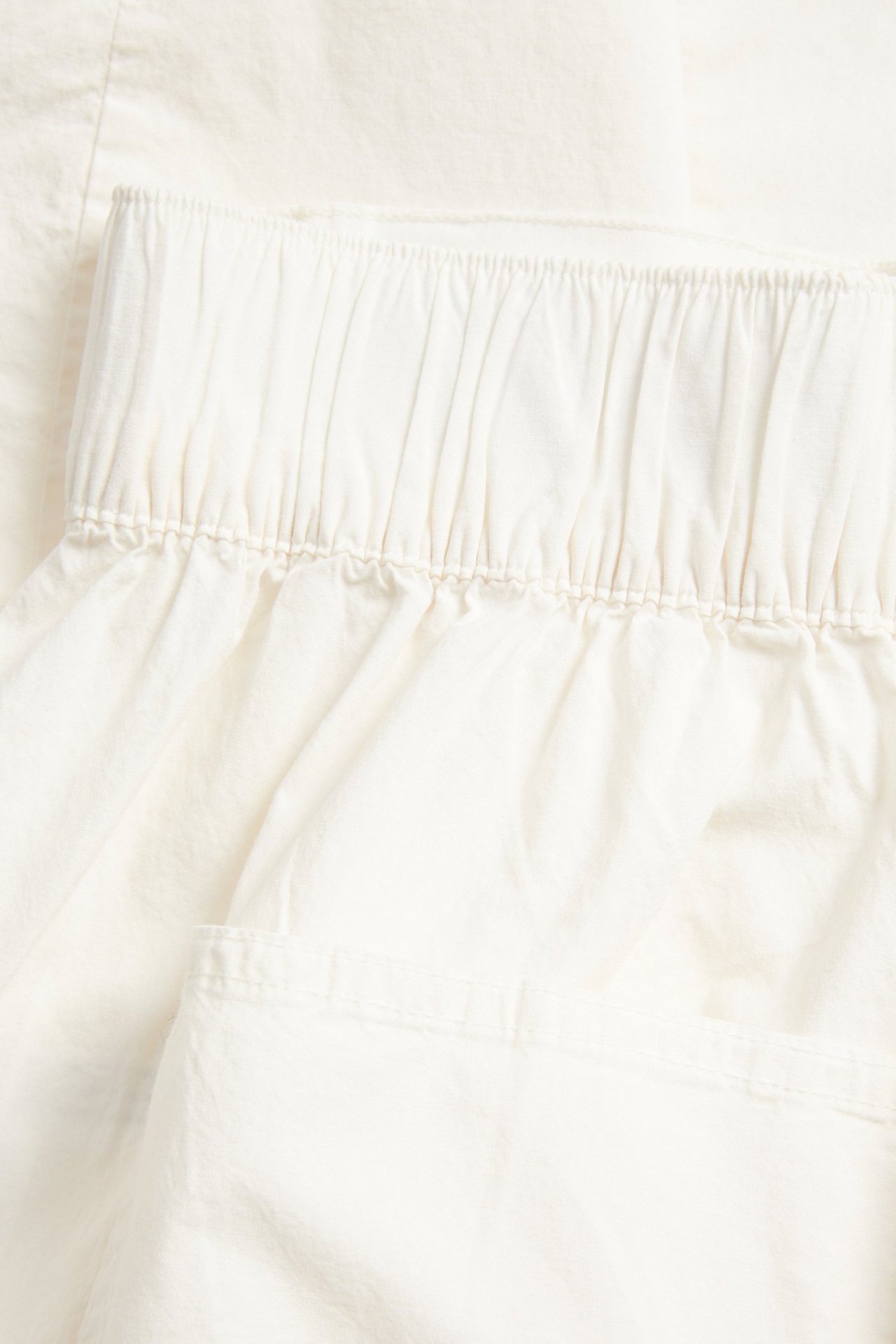 Lähikuva valkoisista popliinihousuista, joissa on joustava vyötärö ja näkyvä sivutasku.