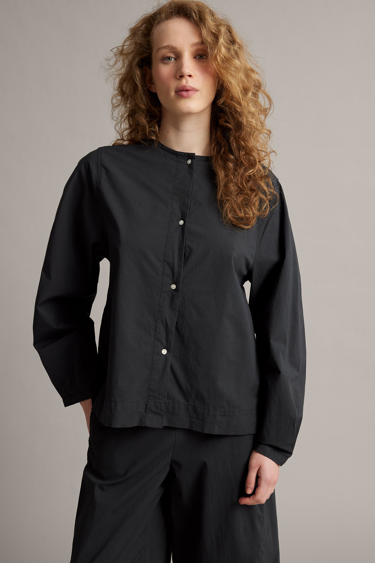 Edestä: Nainen mustassa popliinipuserossa kauluksella, valkoisilla napeilla ja mustilla housuilla.