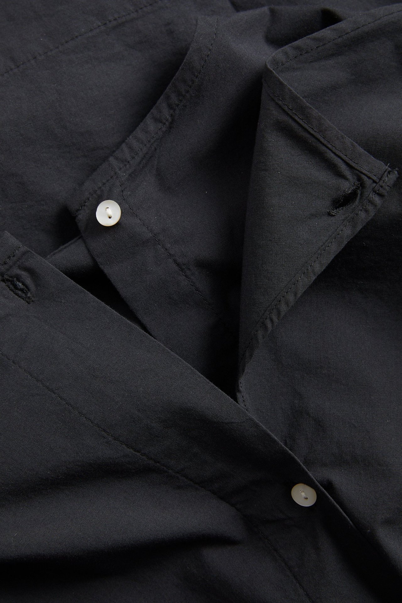 Lähikuva mustasta popliinipuserosta, jossa on kaulus ja valkoiset napit.