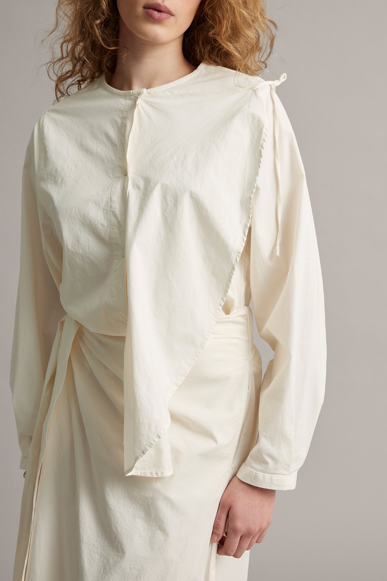 Edestä: Nainen yllään valkoinen popliinipusero, jossa irrotettava röyhelö ja yhteensopiva solmittu hame.