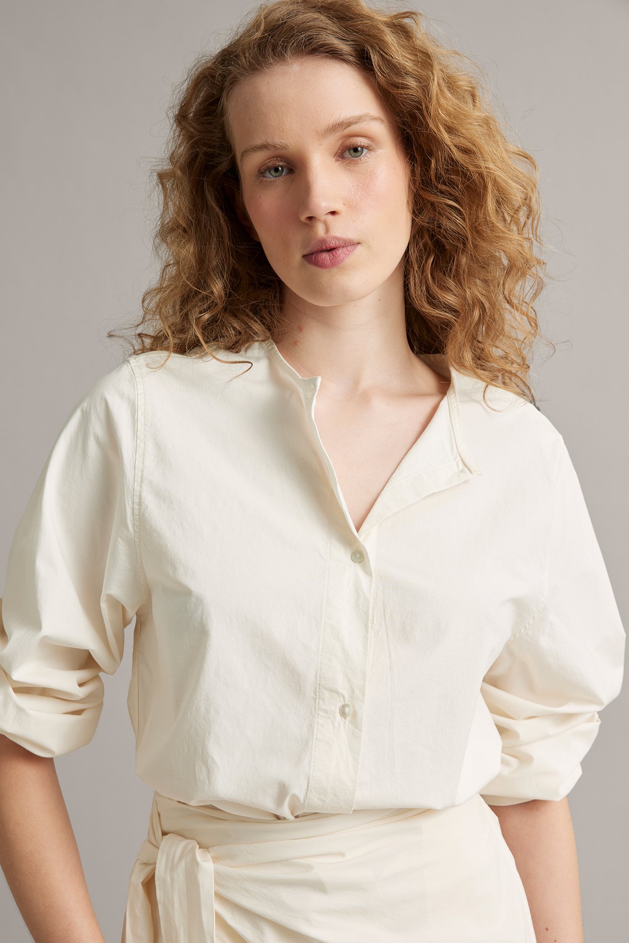 Nainen yllään luonnonvalkoinen popliinipusero V-aukolla, puffihihoilla ja yhteensopiva solmittu kietauluhame.