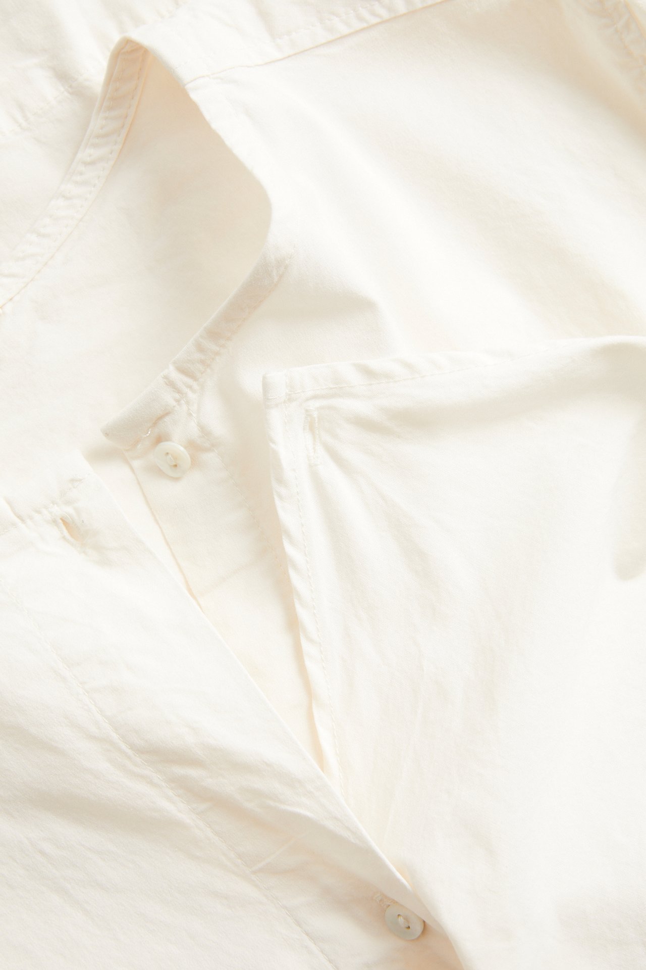 Lähikuva valkoisesta popliinipuserosta, näyttää napit ja kankaan rakenteen.
