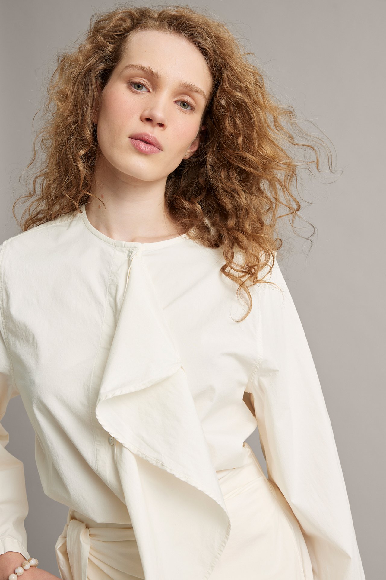 Widok z przodu kobiety w białej bluzce z popeliny z drapowaną falbaną i białymi wiązanymi spodniami.