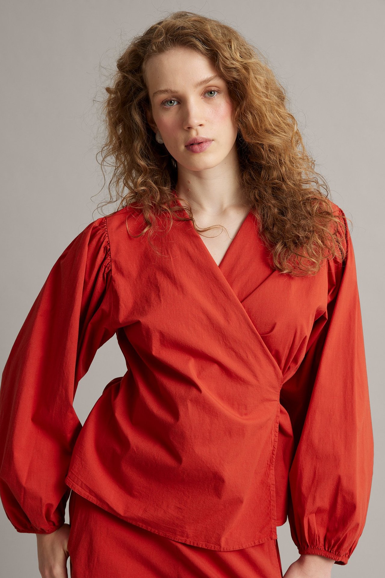 Etukuva: Nainen punaisessa kietaisublousissa pussuhihoilla, joustomudoin, punaisen hameen päällä.