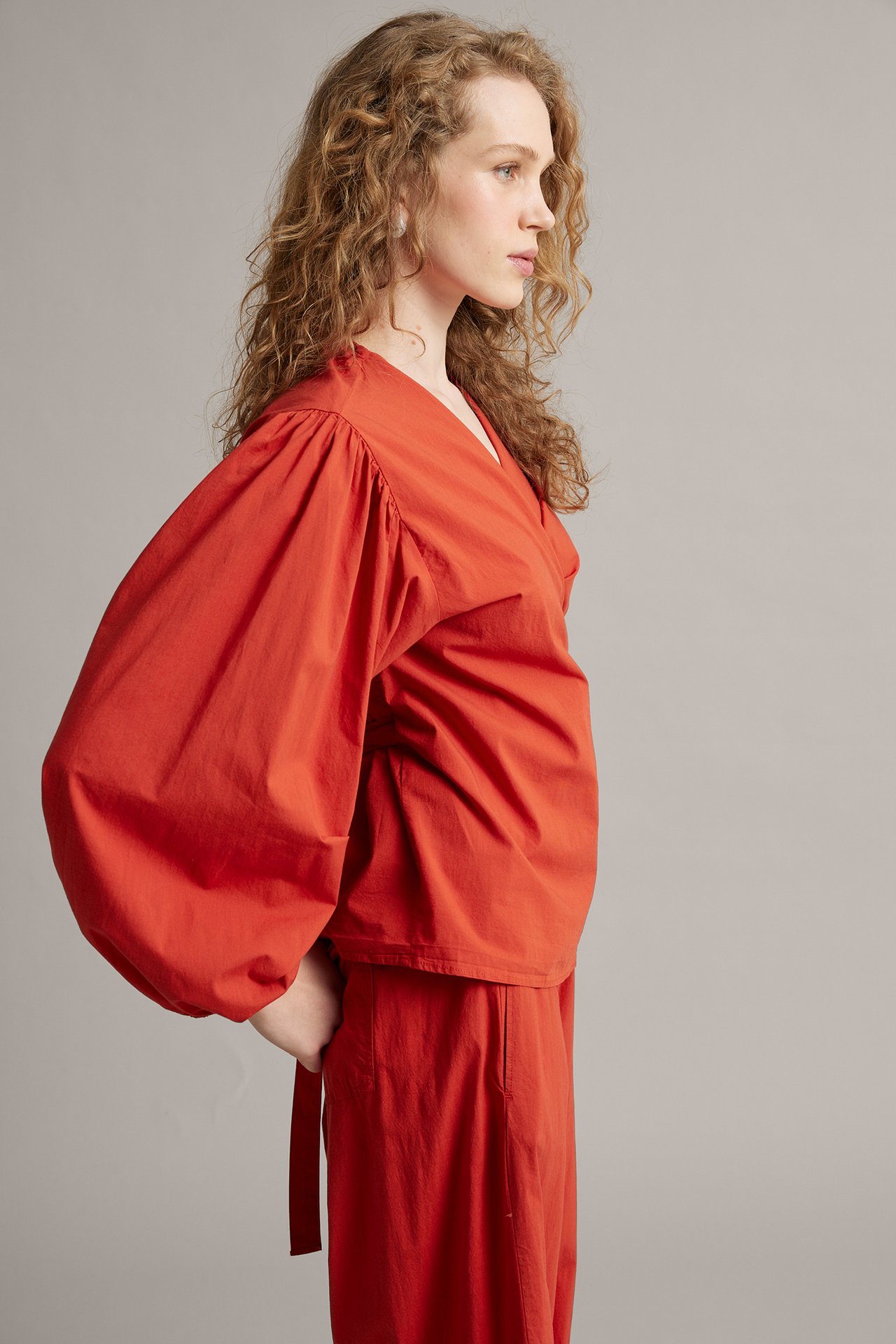 Naisen sivukuva yllään punainen kietaisupusero puhvihihoilla ja yhteensopivat punaiset housut.