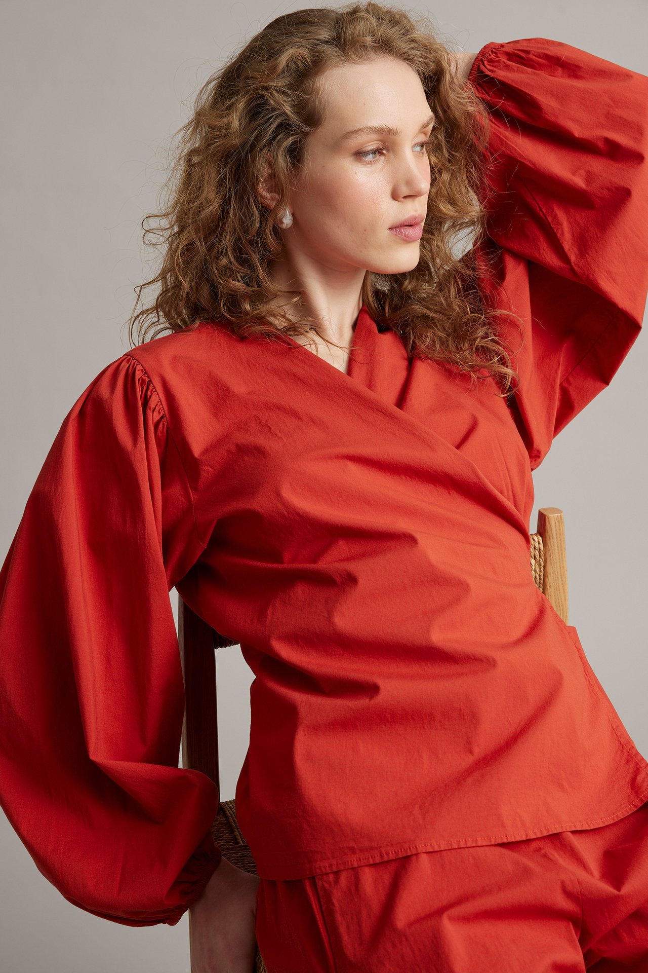 Lähikuva naisesta punaisessa popliini-kietaisublousissa leveillä pussihihoilla ja yhteensopivissa housuissa.