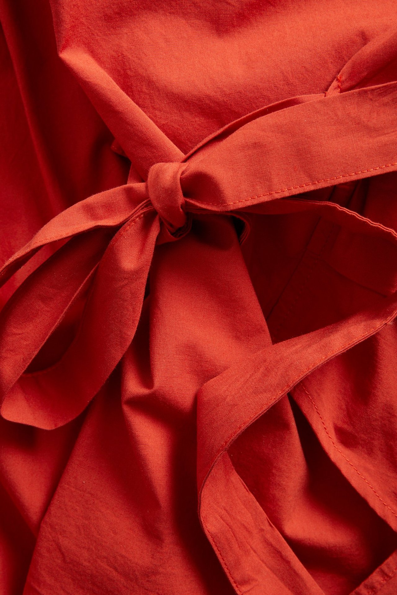Lähikuva punaisesta kietaisupuserosta kudottua popliinia, jossa solmittava yksityiskohta sivulla.