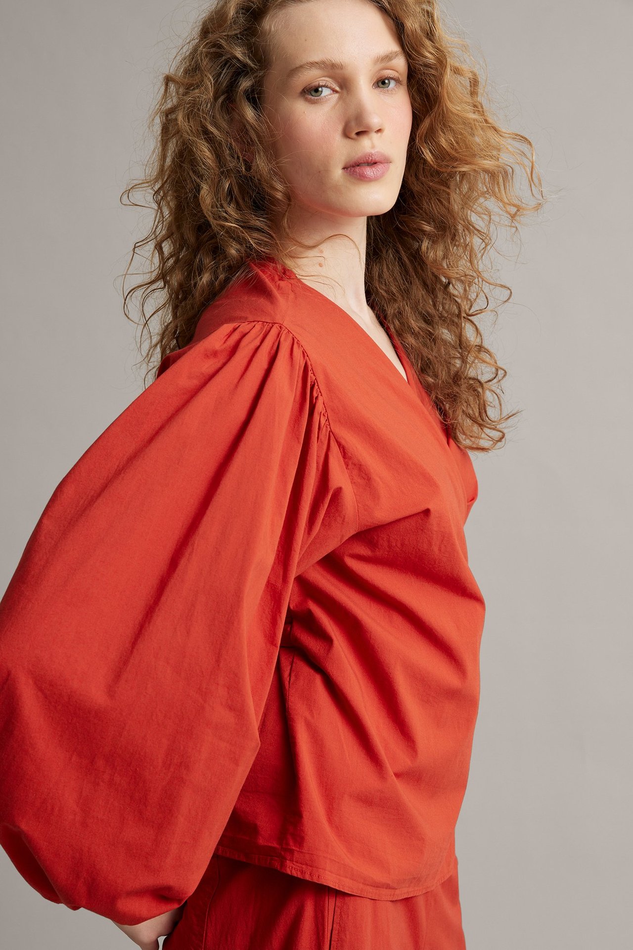 Zbliżenie kobiety w czerwonej bluzce kopertowej z bufiastymi rękawami, elastycznymi mankietami i pasującymi spodniami.