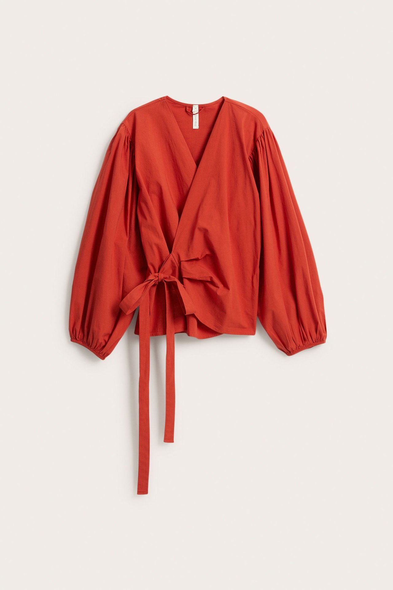 Edestä näkymä ruosteenpunaisesta kietaisubluzista, jossa leveät pussihihat ja solmu sivulla.