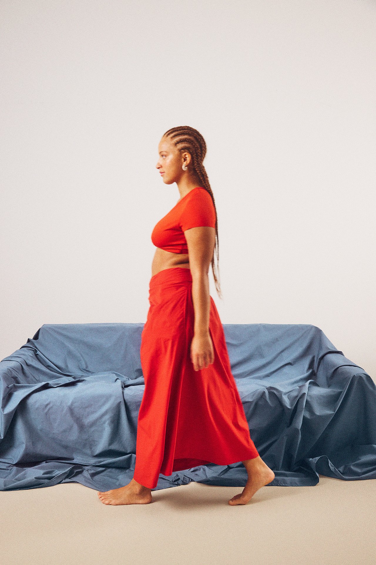 Kobieta w czerwonej popelinowej spódnicy kopertowej z wiązaniem, czerwonym crop topie i białych kolczykach, widok z boku.