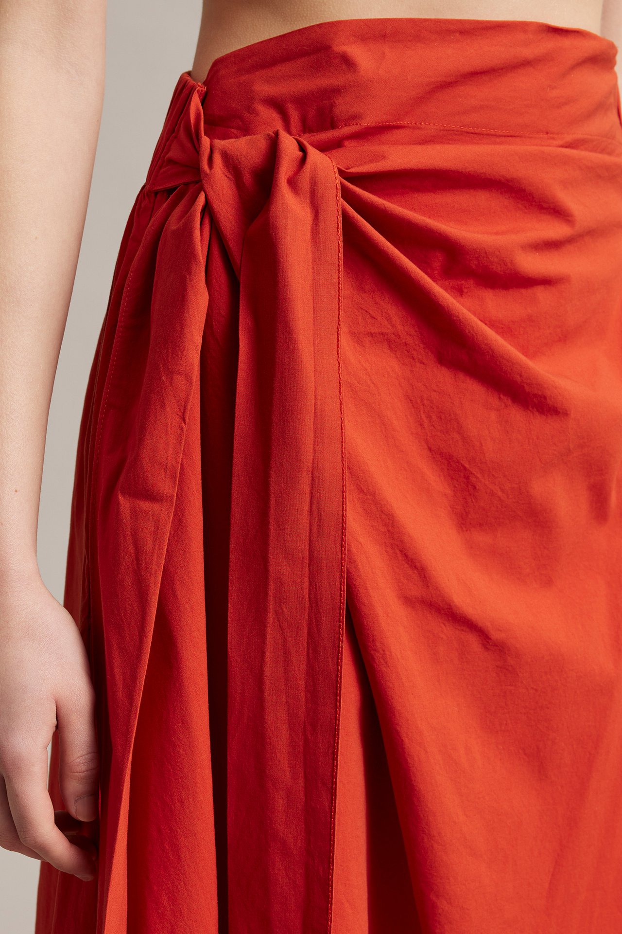 Nærbilde av kvinne iført et rødt A-formet omslagsskjørt i poplin med knyting i siden.