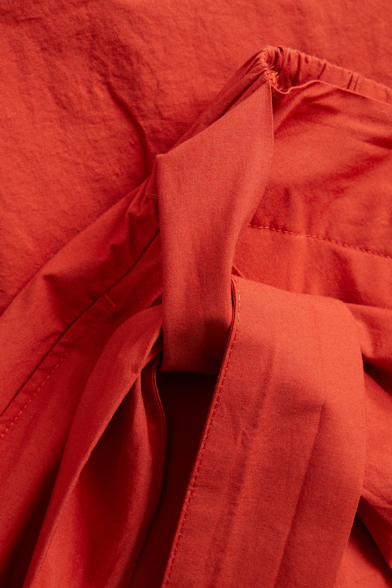 Lähikuva punaisesta popliinihameesta, jossa kietaisumalli, sivusolmu ja joustava vyötärönauha takana.