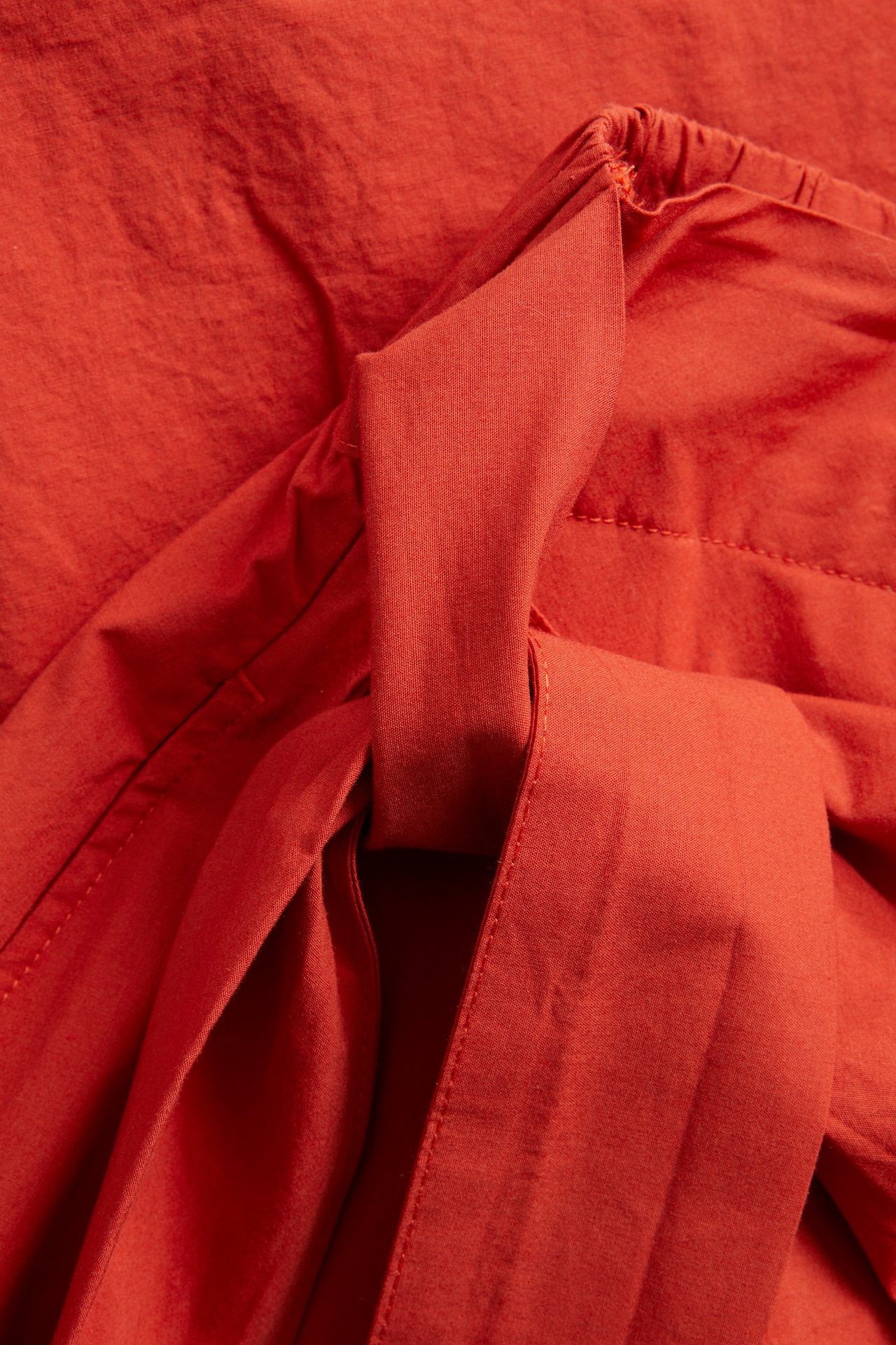 Lähikuva punaisesta popliinihameesta, jossa kietaisumalli, sivusolmu ja joustava vyötärönauha takana.