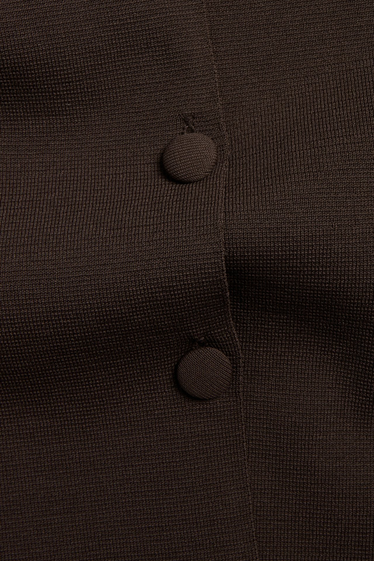 Nærbilde av en mørkebrun, ensfarget strikket cardigan med to synlige knapper.