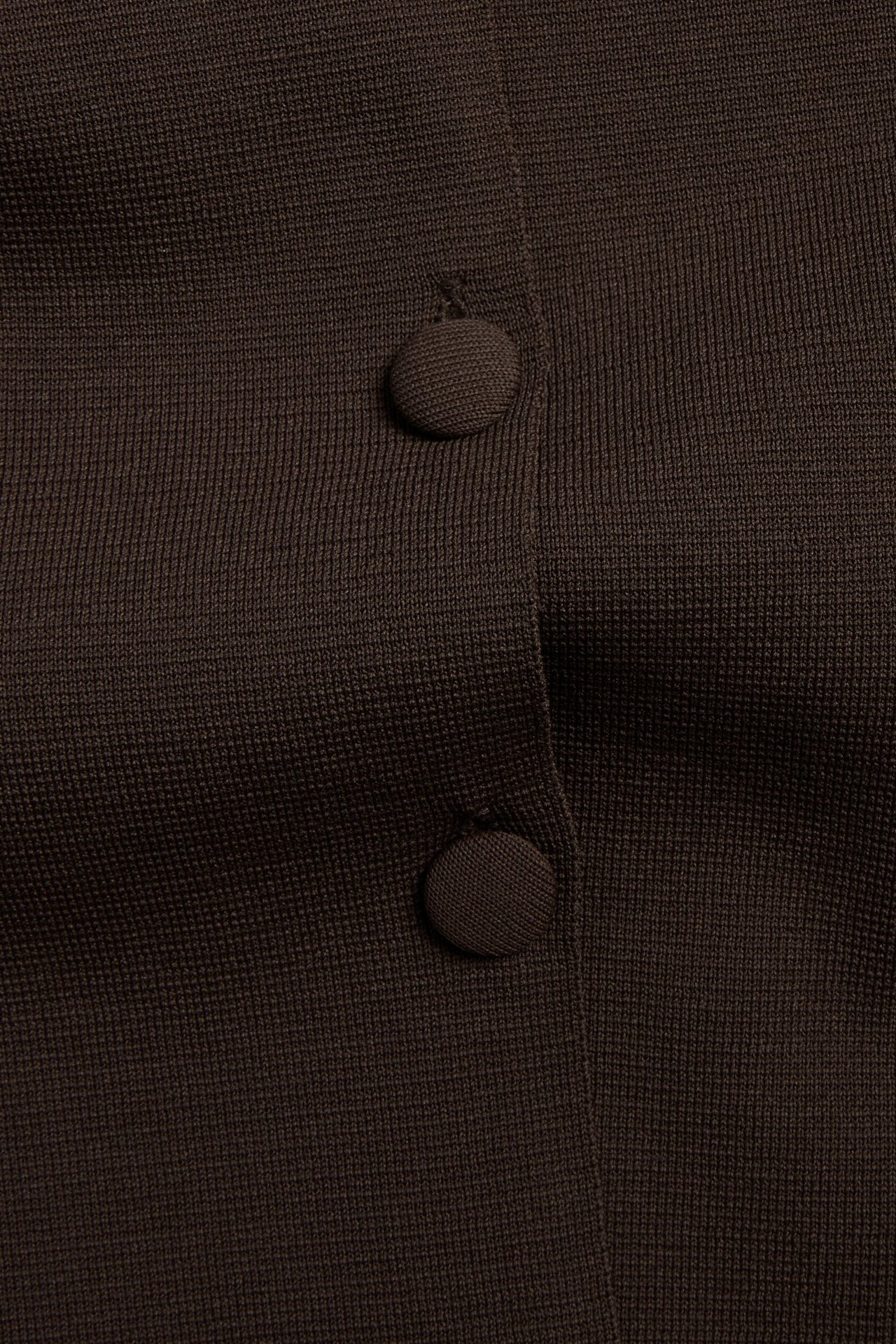 Zbliżenie ciemnobrązowego, gładkiego kardiganu z dzianiny z dwoma widocznymi guzikami.