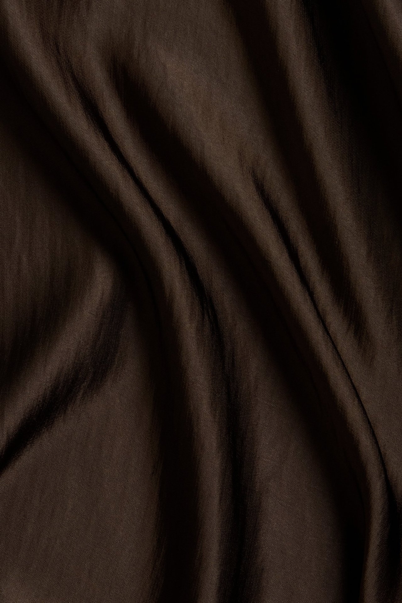 Närbild på tyget av en mörkbrun klockad satinkjol med mjuka veck.
