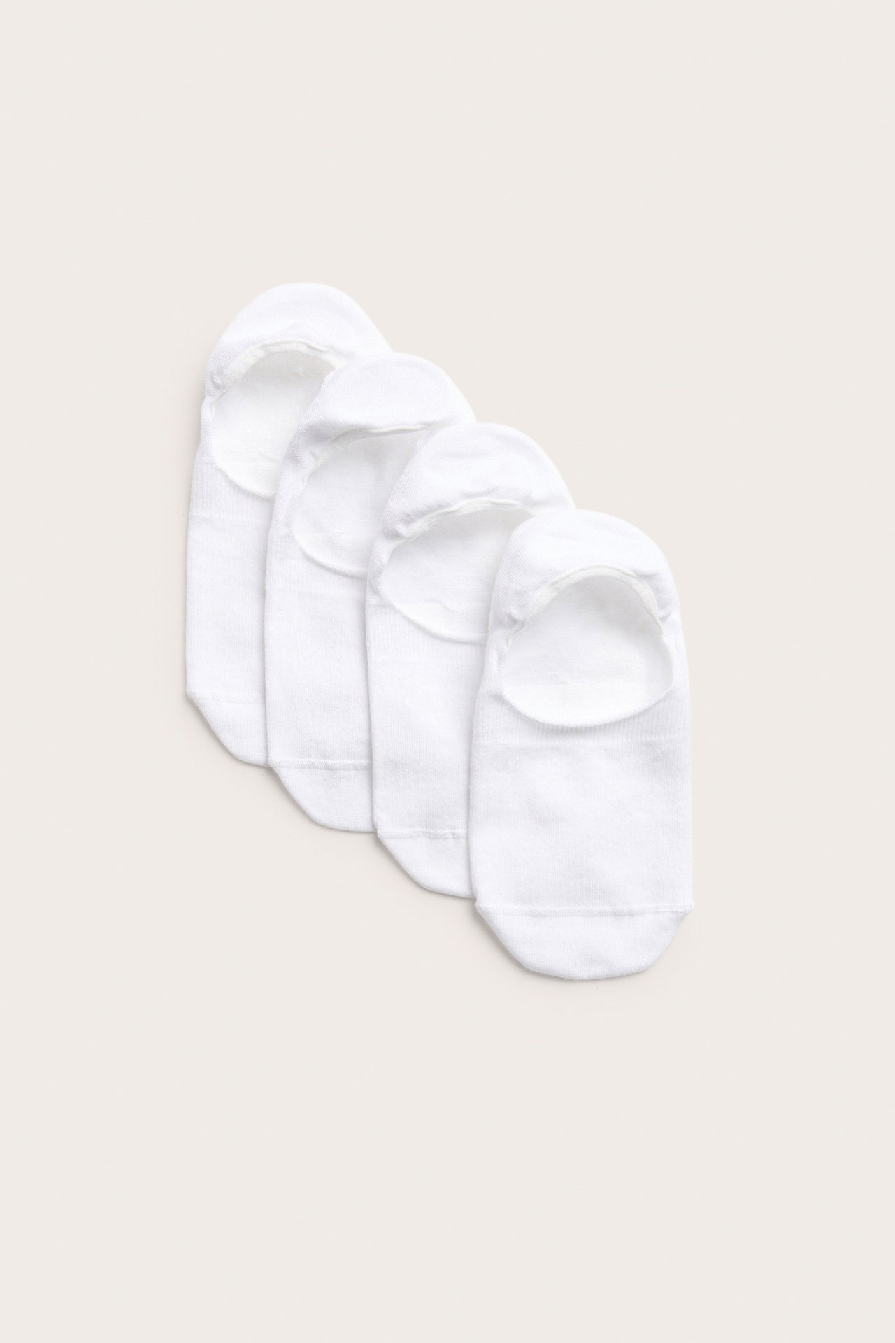 Toppvy av fyra vita enfärgade sneakerstrumpor i bomullsmix med silikongrepp i hälen.