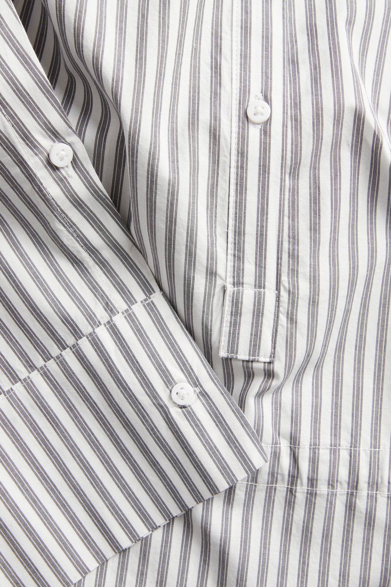 Närbild av en offwhite och grårandig bomullsskjorta med synliga vita knappar på knäppslå och manschett.