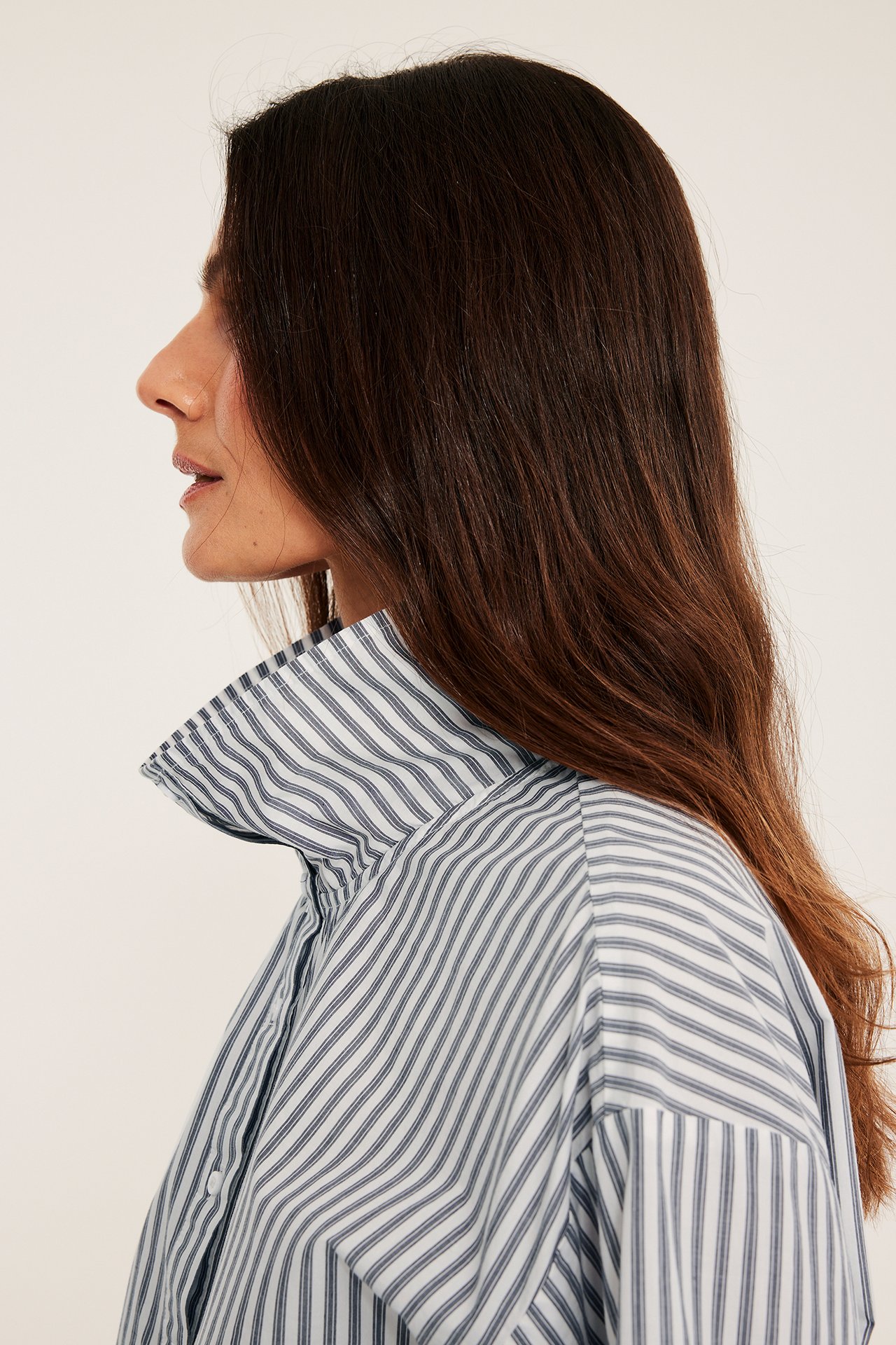 Närbild i sidoprofil av en kvinna som bär en offwhite- och blårandig bomullsskjorta med ståkrage.