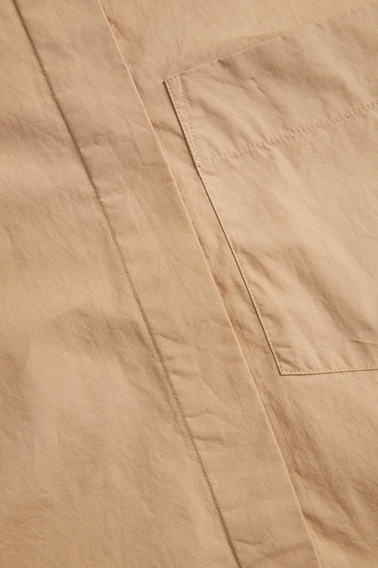 Nærbilde av en beige kortermet skjorte i bomullspoplin med brystlomme og skjult knepping.