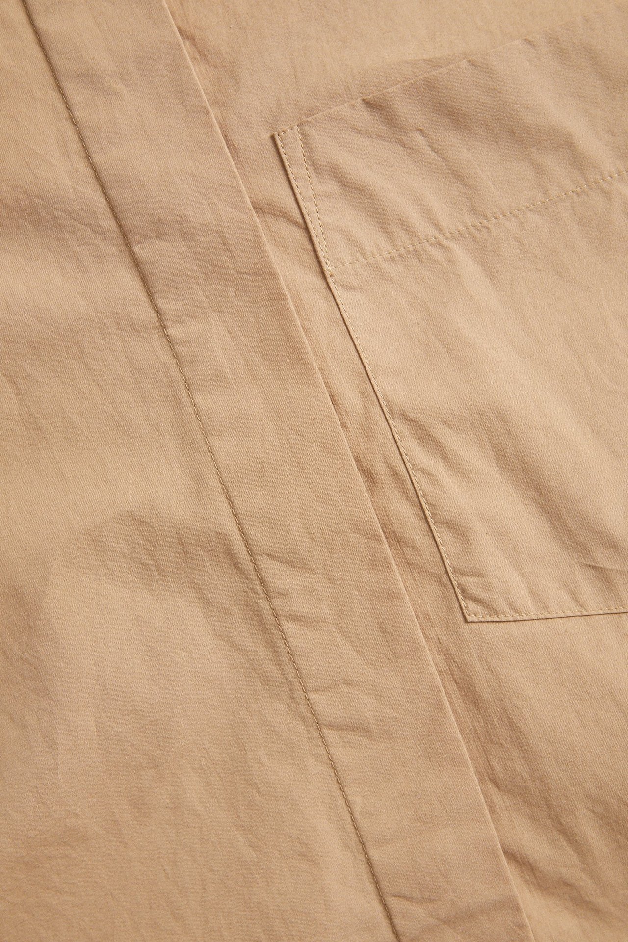 Nærbilde av en beige kortermet skjorte i bomullspoplin med brystlomme og skjult knepping.