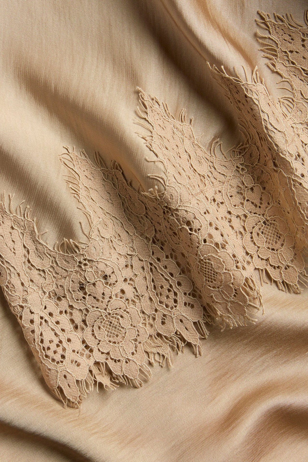 Zbliżenie na jasnobrązową satynową spódnicę z misterną koronkową krawędzią w kwiaty.