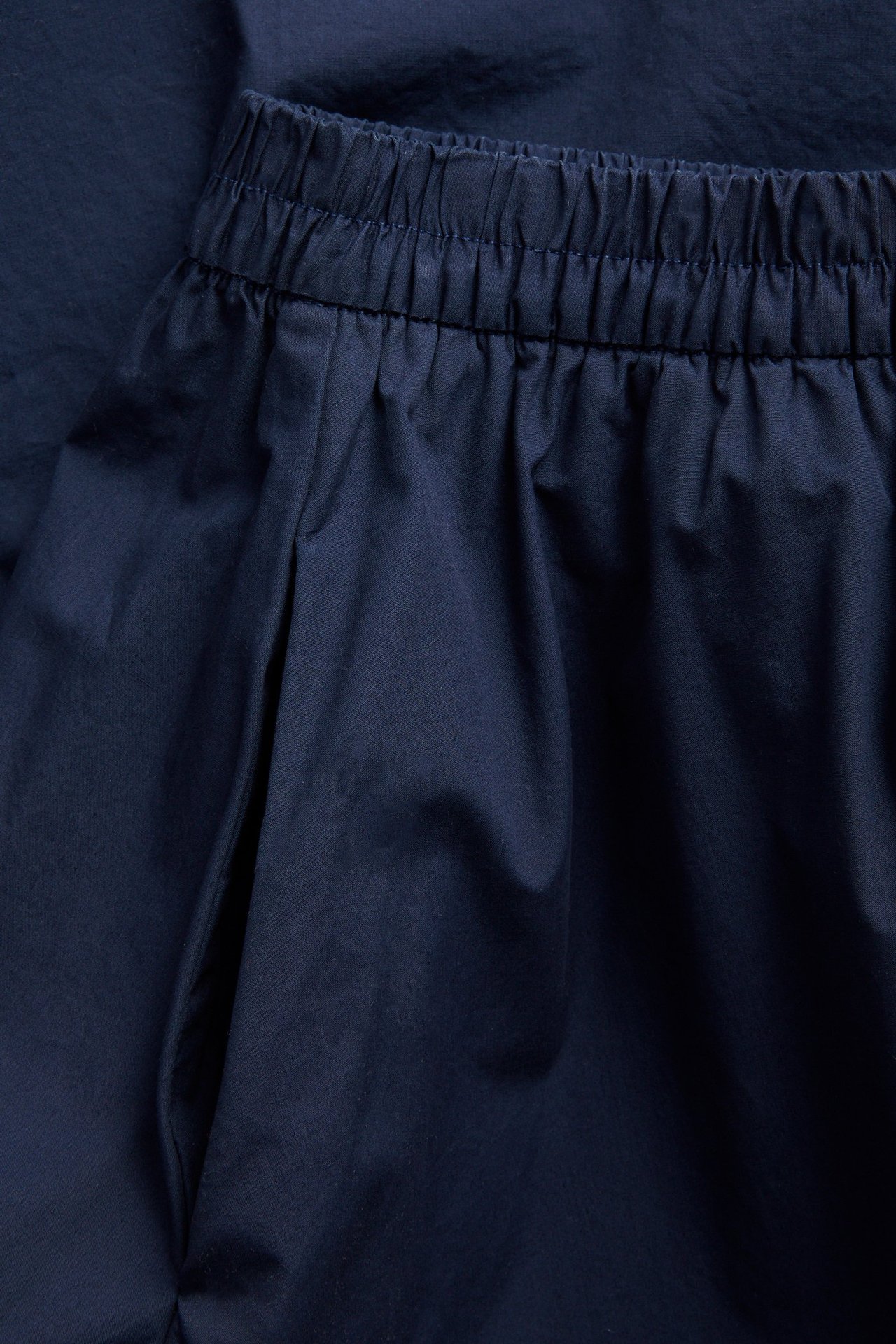 Nærbilde forfra av et mørkeblått utsvingt poplinskjørt i bomull med elastisk midje og sidelomme.