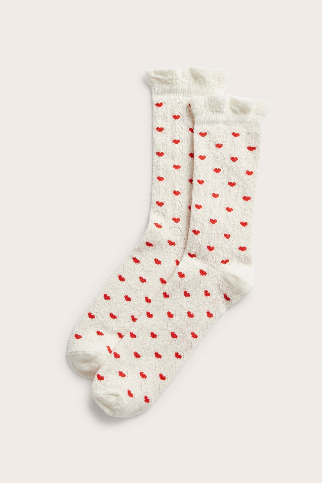 Ovenfra to offwhite pointelle-sokker med røde hjertemønstre og bølgete øvre kanter.