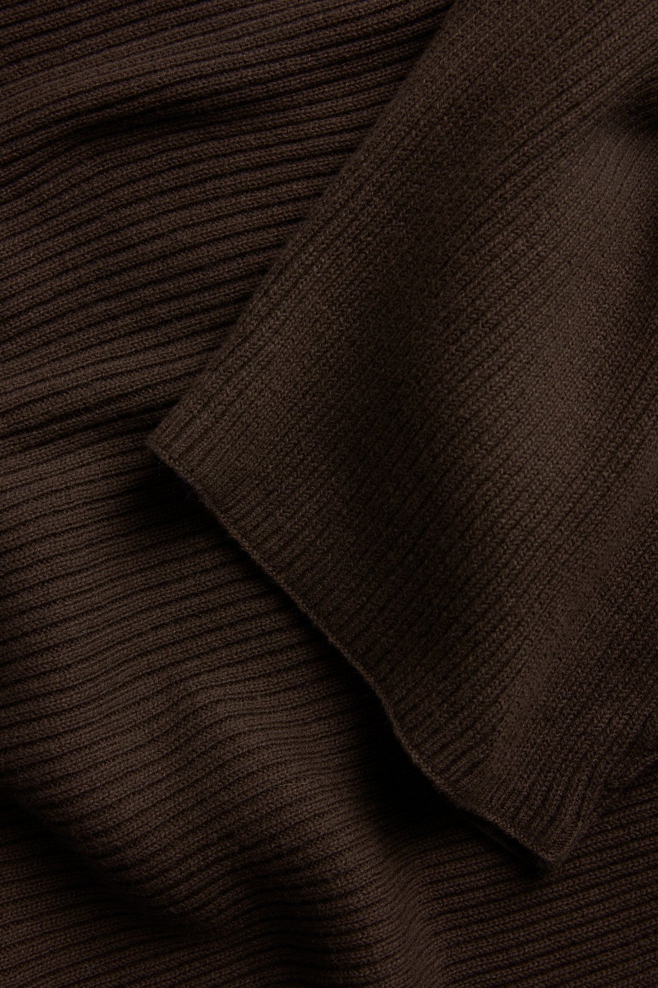 Nærbilde av en mørkebrun, ribbestrikket genser i 100% bomull, med synlige folder i stoffet.