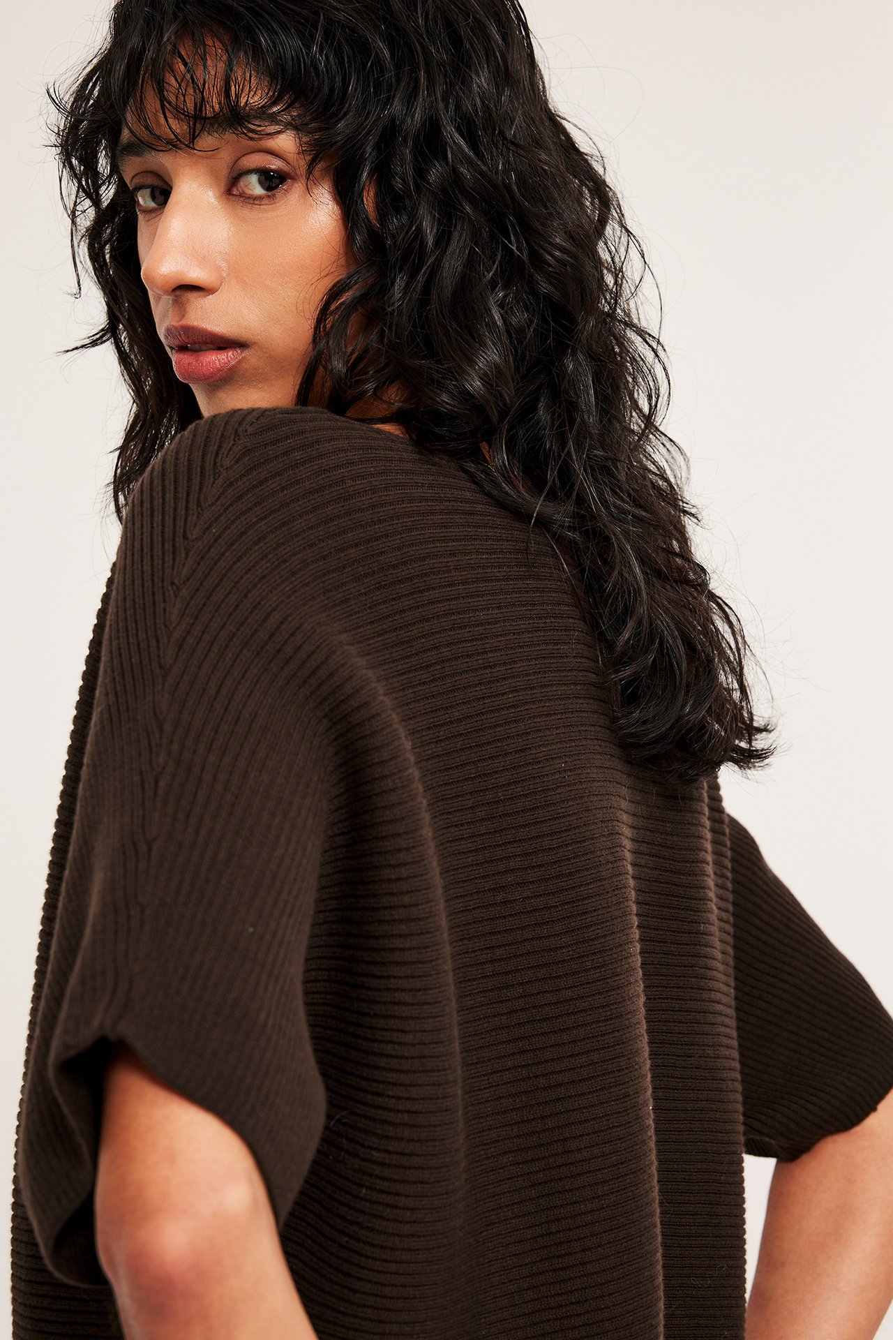 Nainen yllään tummanruskea ribbineuleinen lyhythihainen villapaita takaa.