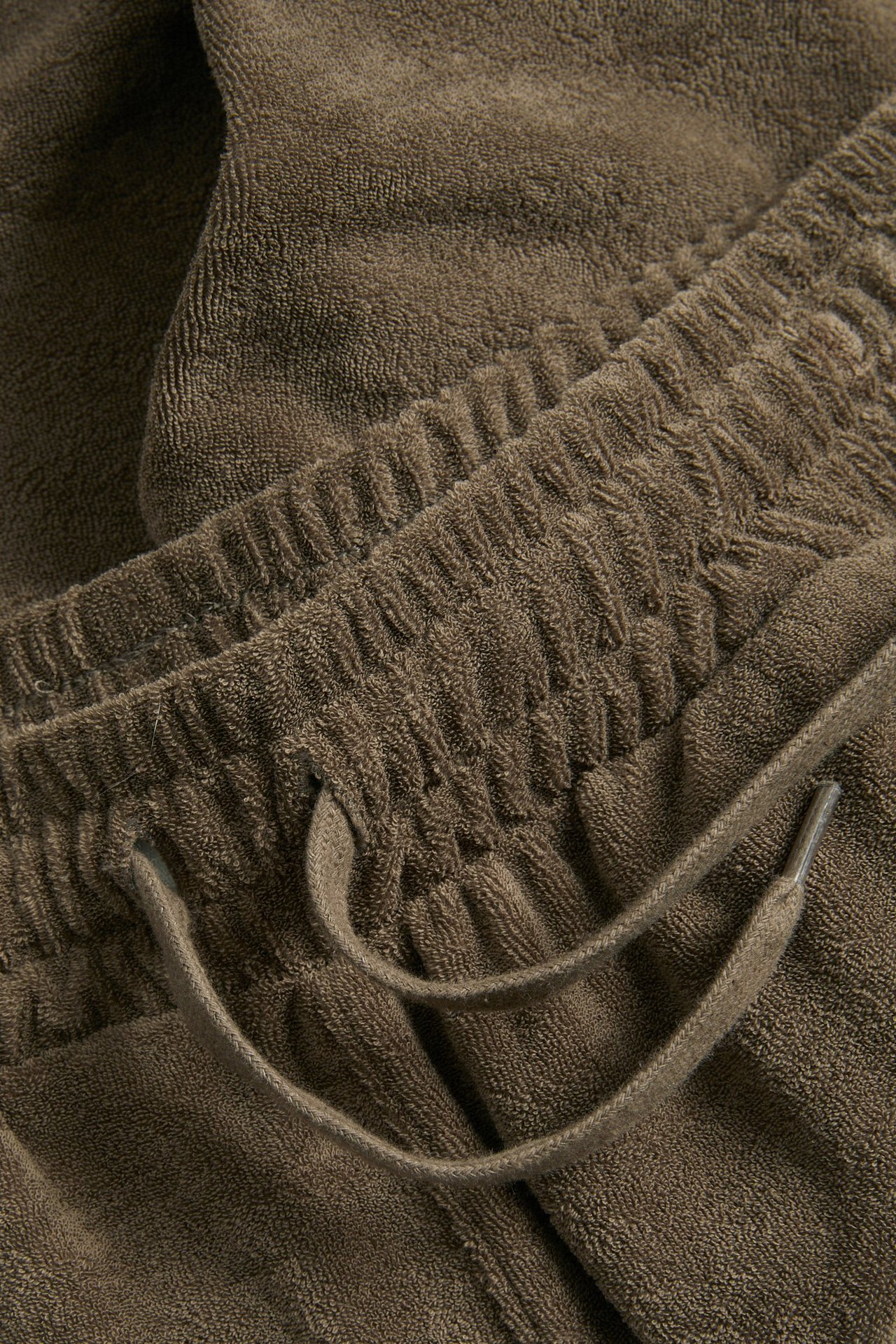 Lähikuva ruskeista froteeshortseista, joissa joustava vyötärö ja toiminnallinen kiristysnyöri.