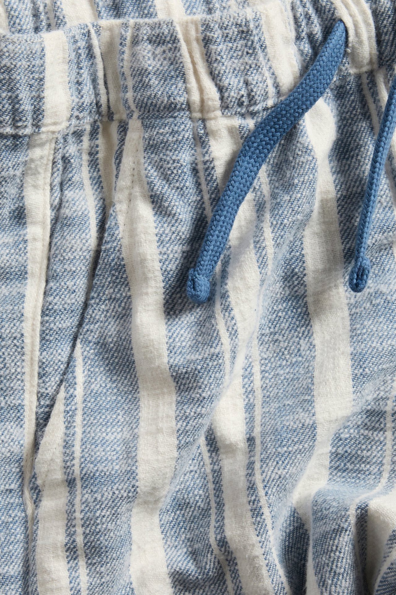 Zbliżenie na niebiesko-białe szorty w paski z elastyczną talią i niebieskim sznurkiem.