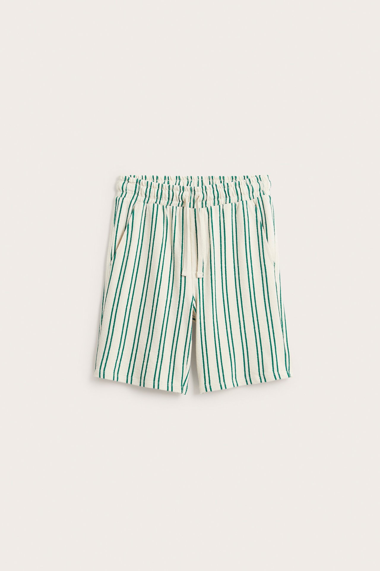 Framsida av vita bomullstickade shorts med gröna ränder, elastisk dragsko i midjan och sidfickor.