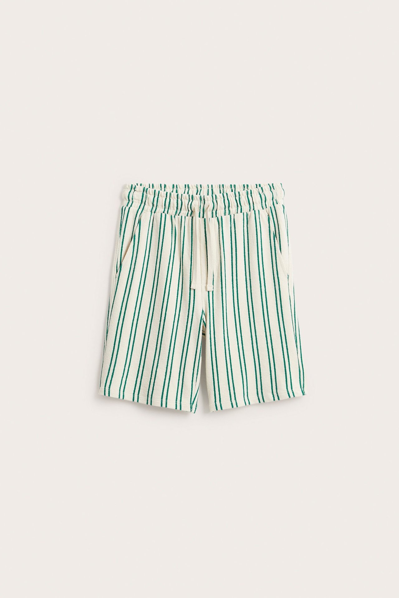 Edestä: valkoiset puuvillaneuloshortsit vihreillä raidoilla, joustava kiristysnyörivyötärö ja sivutaskut.