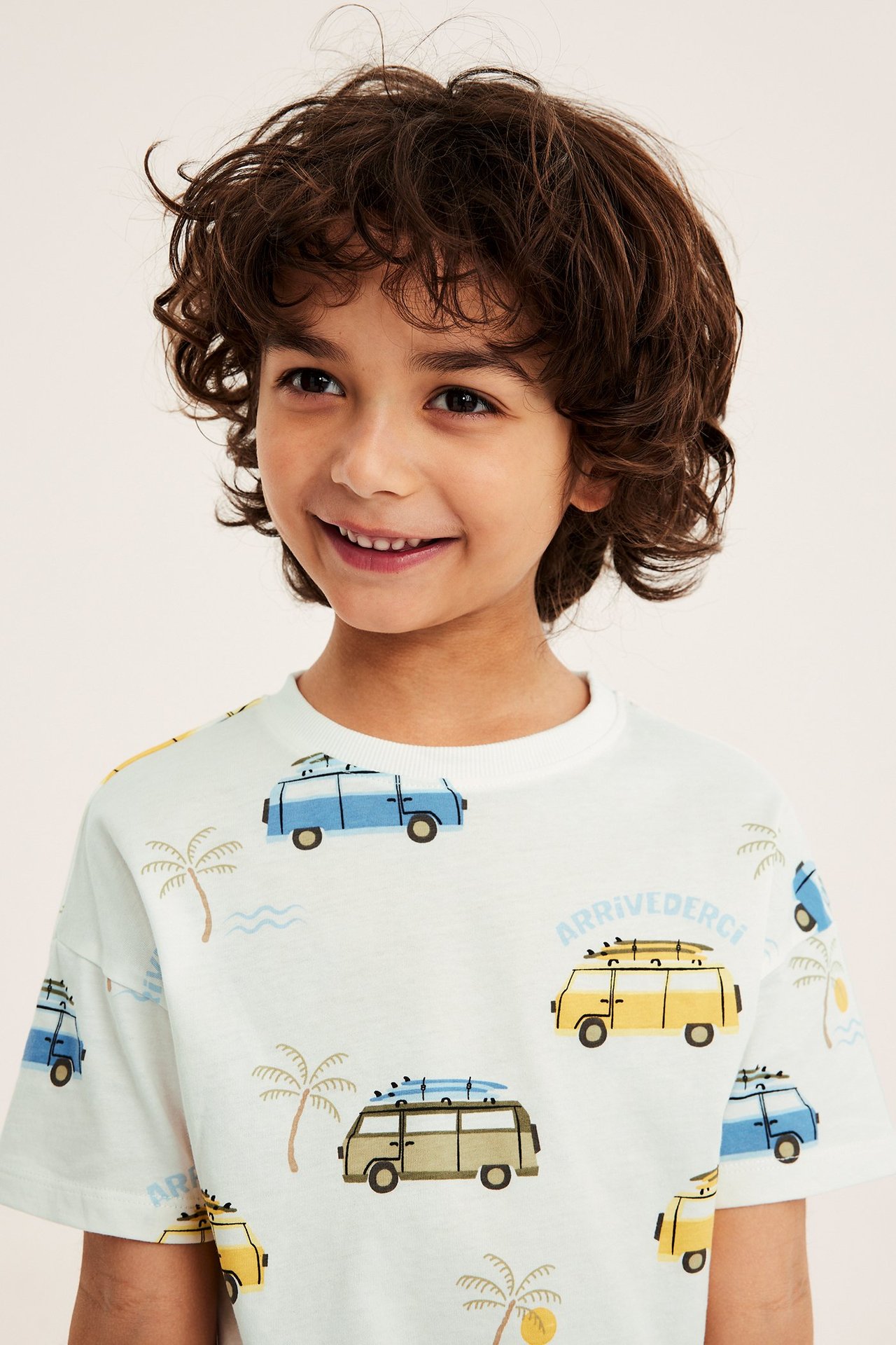 Närbild framifrån på ett barn i en offwhite bomulls-t-shirt med tryck av blå och gula husbilar.