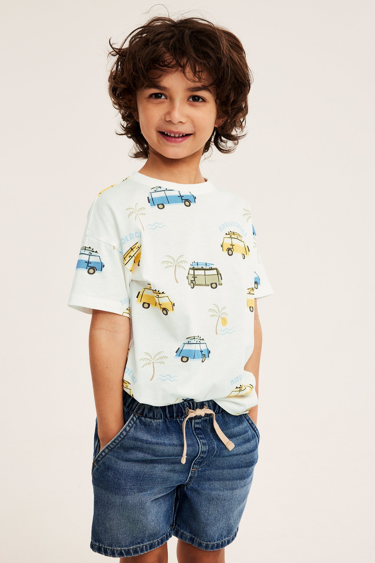 Frontvisning av et barn i offwhite bomulls-T-skjorte med van-print og blå denimshorts.
