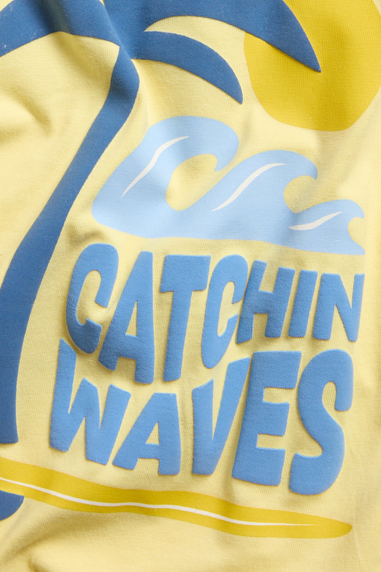 Zbliżenie na żółtą bawełnianą bluzę niemowlęcą z nadrukiem 'Catchin Waves', palmą, falami.