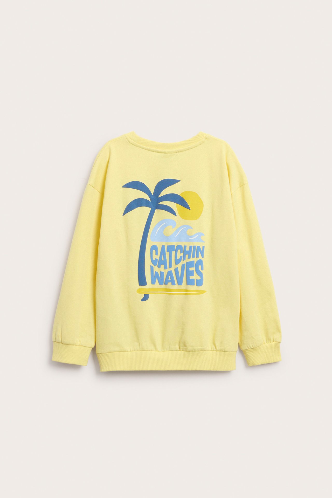 Lapsen keltainen puuvillasweatshirt, jossa sininen palmu ja 'CATCHIN WAVES' -tekstiprintti takana.