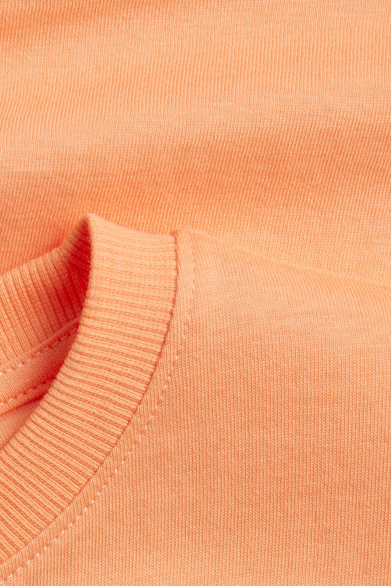Närbild på en orange mjuk t-shirt i bomullstrikå, med ribbad rund halsringning.