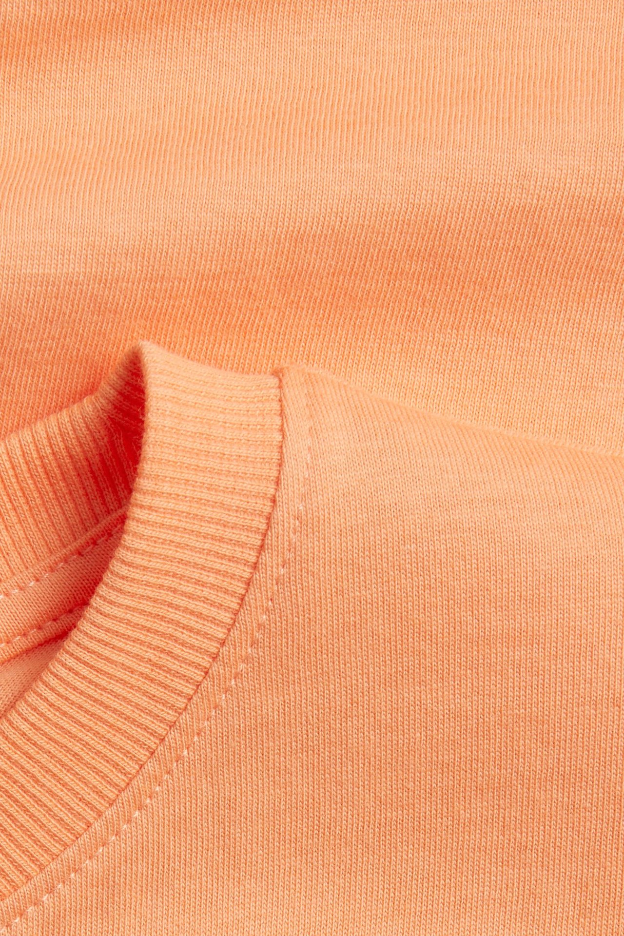 Zbliżenie pomarańczowego, miękkiego T-shirtu z dzianiny bawełnianej z prążkowanym okrągłym dekoltem.