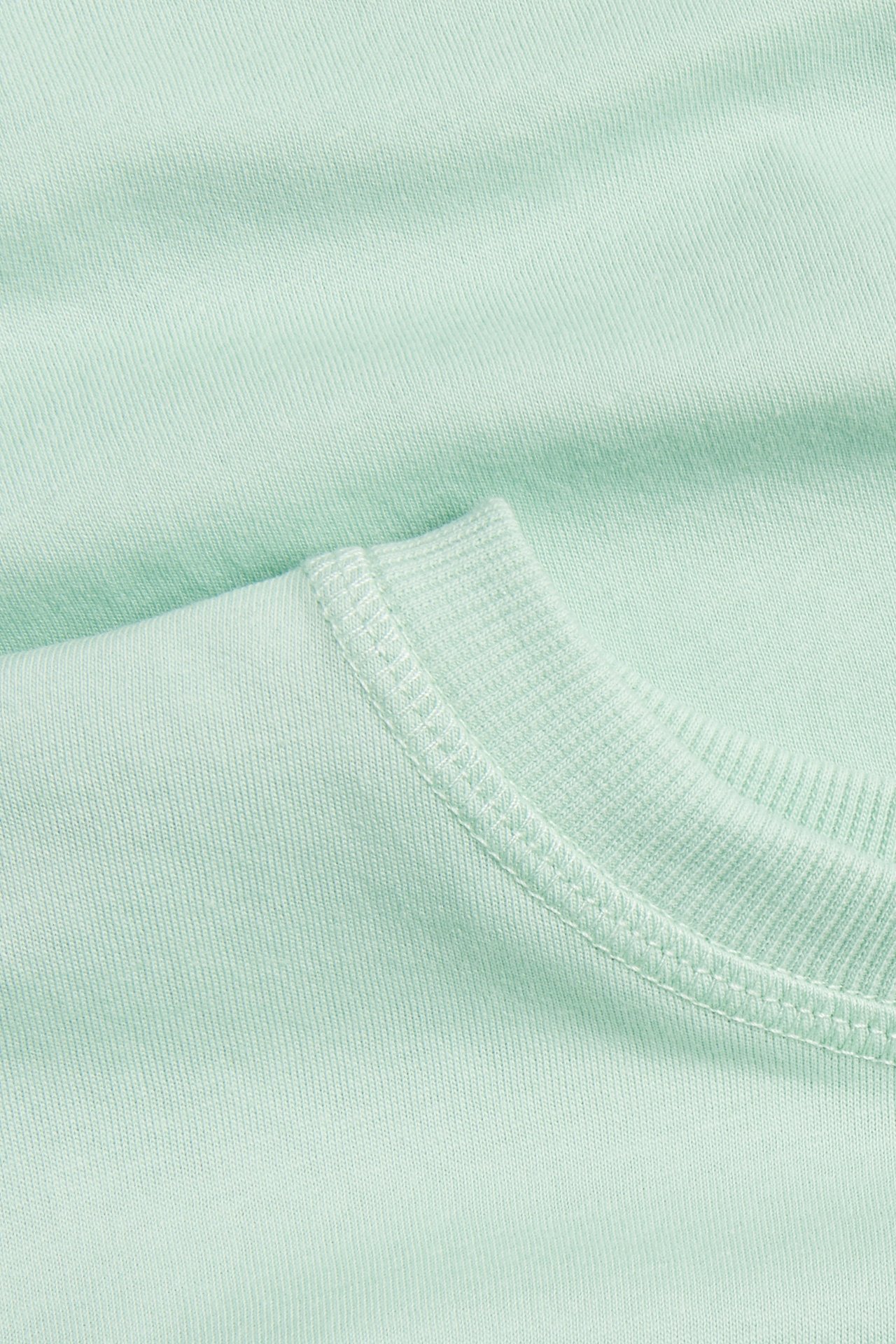 Zbliżenie na jasnozielony bawełniany T-shirt z prążkowanym dekoltem i widocznymi szwami.